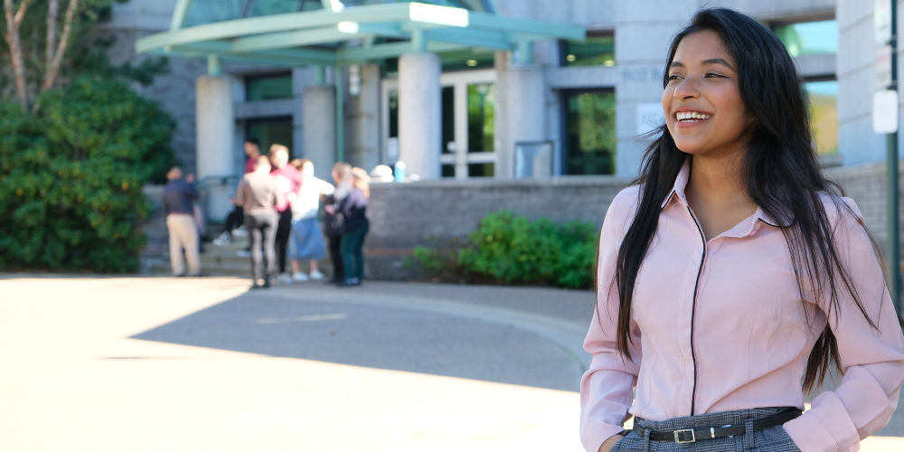 Female student stands with hands in pockets in front of Sobey building.