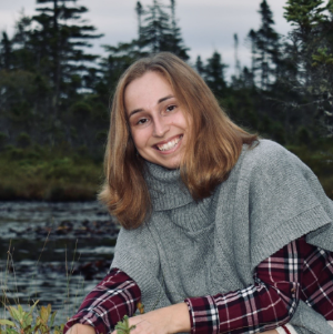 A woman posing for a photo in front of some trees and a lake