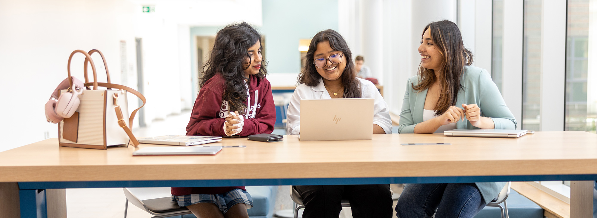 Three students looking at a laptop in a large room.