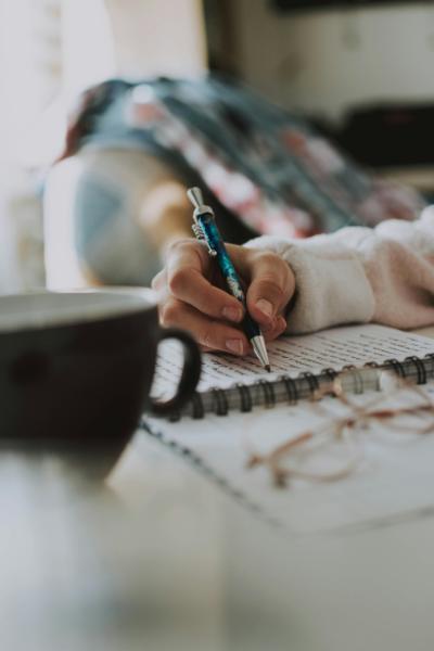 Photo of a woman writing in a notebook with a mug of coffee