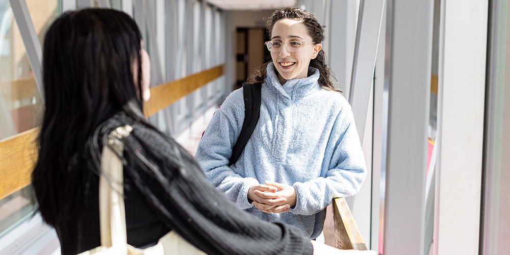 Two people chatting in glassed-in walkway.