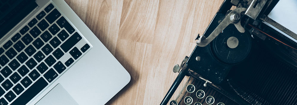 A laptop computer beside a typewriter.