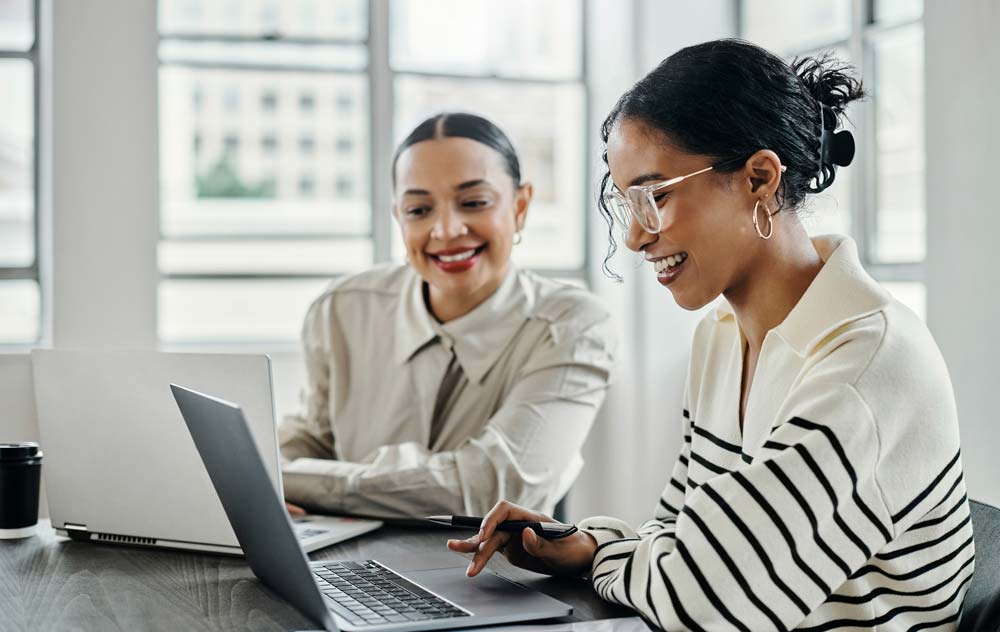 Two women sitting at a desk viewing a laptop